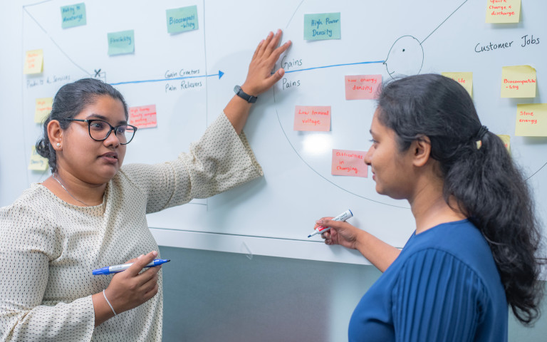 Two John Keells female researchers brainstorming in-front of a white board with sticky notes